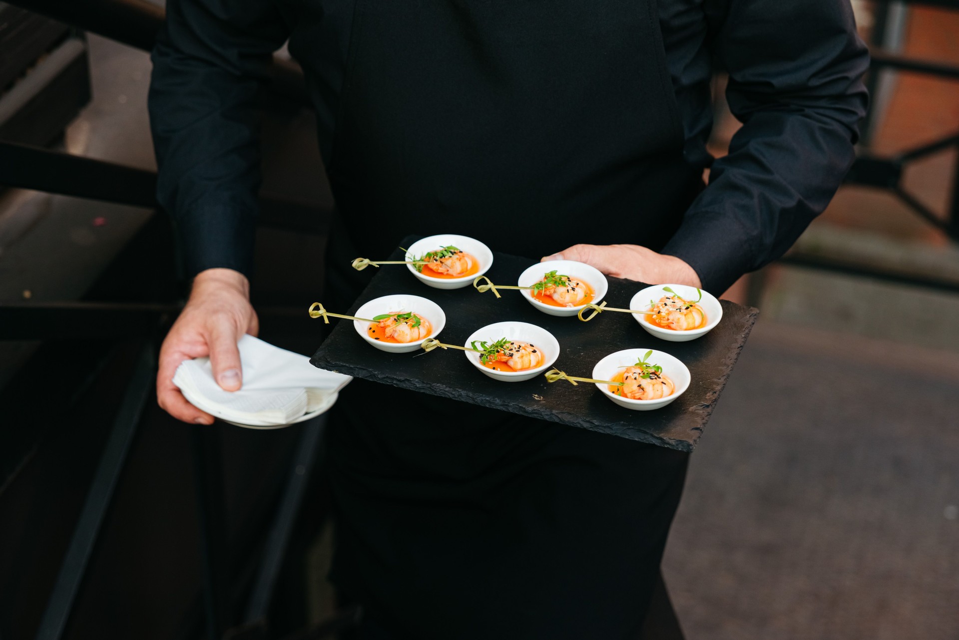 Waiter serving gourmet shrimp appetizers at event.