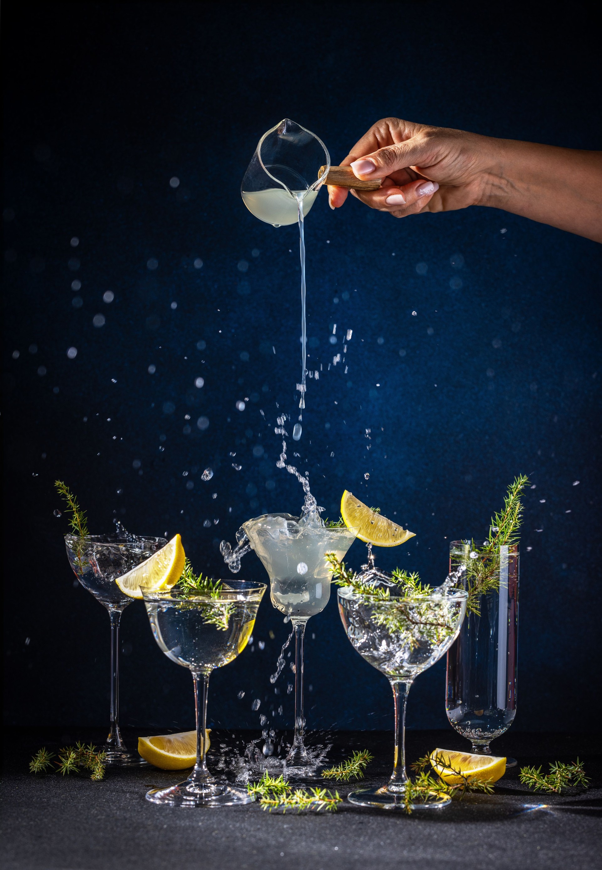 Le barman verse du gin dans des verres à cocktail avec du citron et des baies de genièvre, créant un effet d’éclaboussure Le barman verse du gin dans des verres à cocktail avec du citron et des baies de genièvre, créant un effet d’éclaboussure